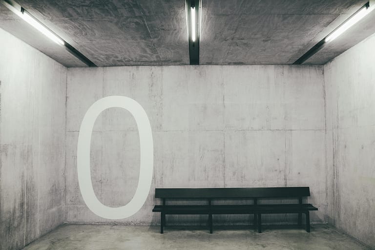 Un 0 est peint sur un mur en blanc a coté d'un banc dans un parking